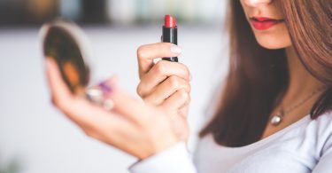 Retusche beim Bewerbungsfoto, Frau steht mit rotem Lippenstift in der Hand vor dem Spiegel